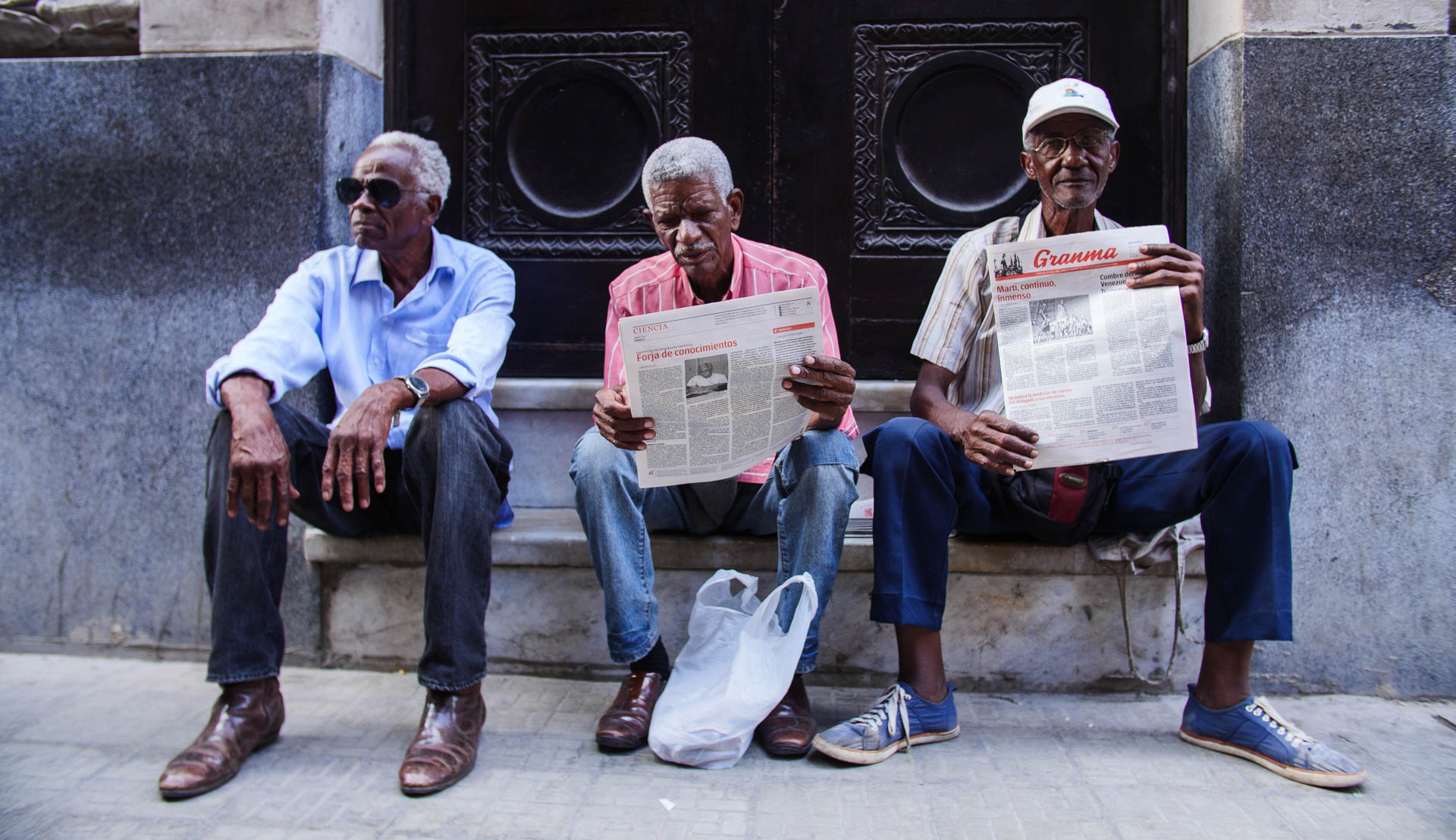 Three men sitting together on stone steps with newspapers